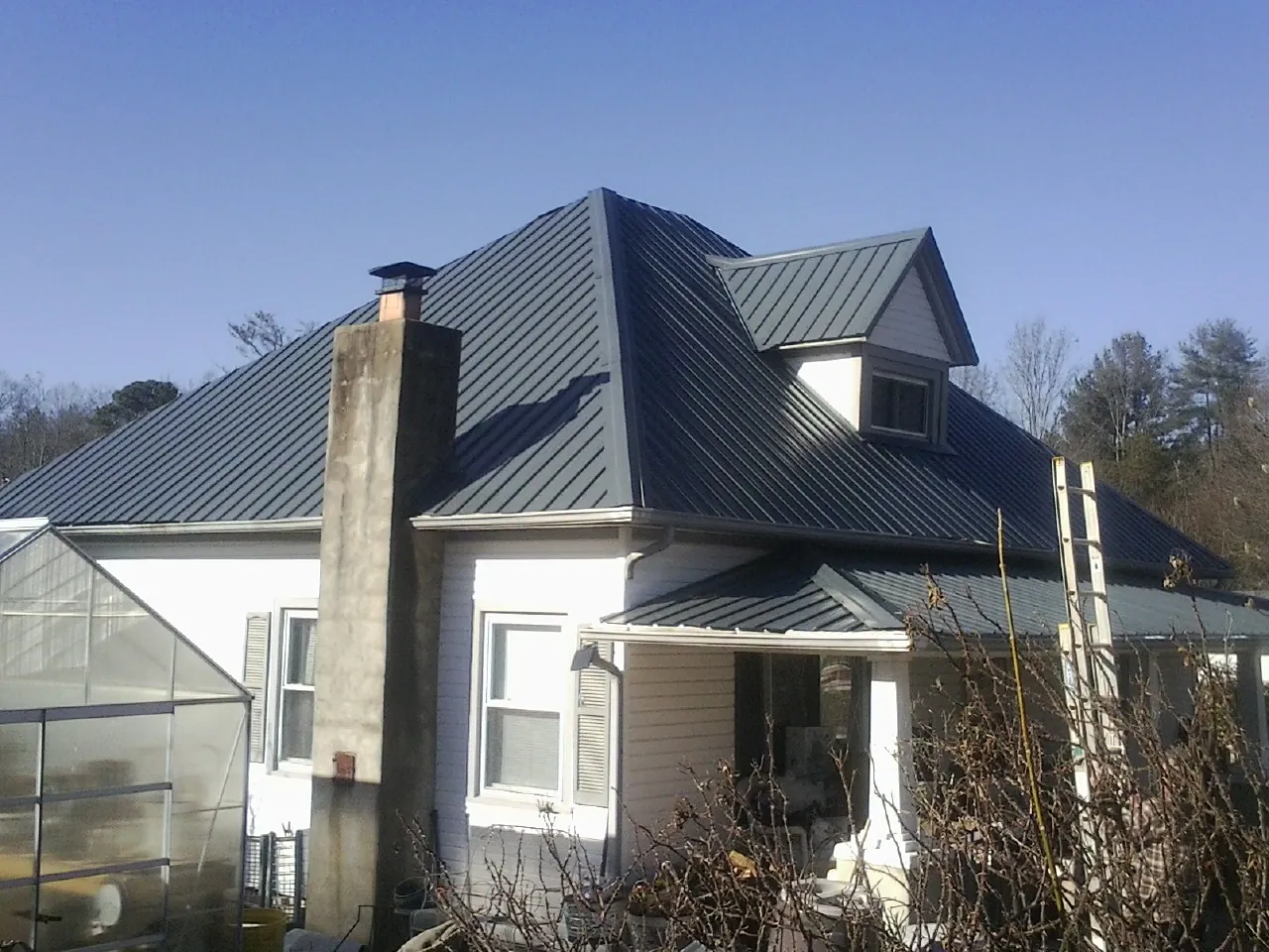 Dark blue standing seam metal roof on a white farmhouse with dormer — Slate & Tile Roof Repair by Roofing Brothers in Mabelvale