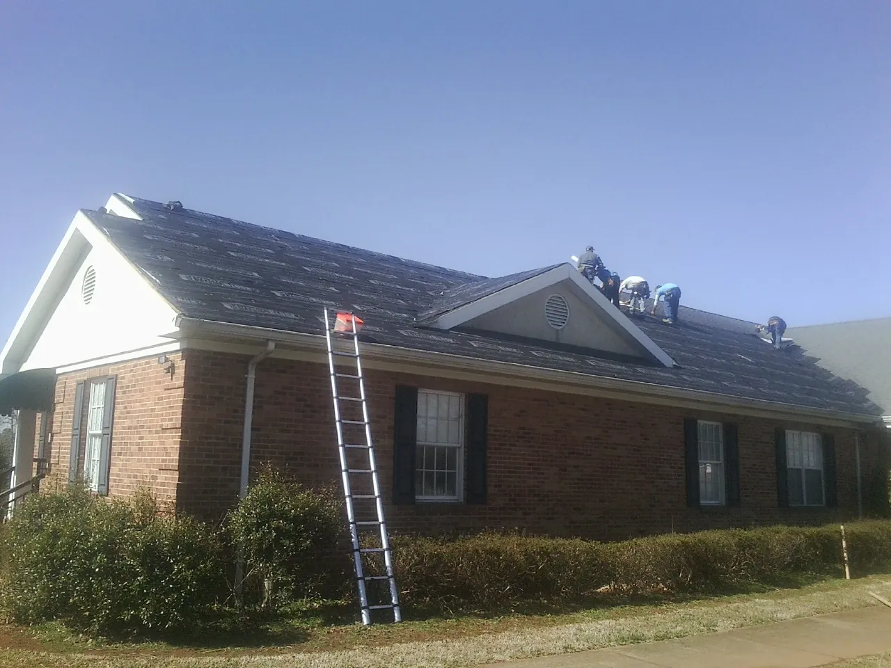 Crew tearing shingles off a brick ranch roof with a ladder set — Emergency Roof Repair work by our crew in Mabelvale