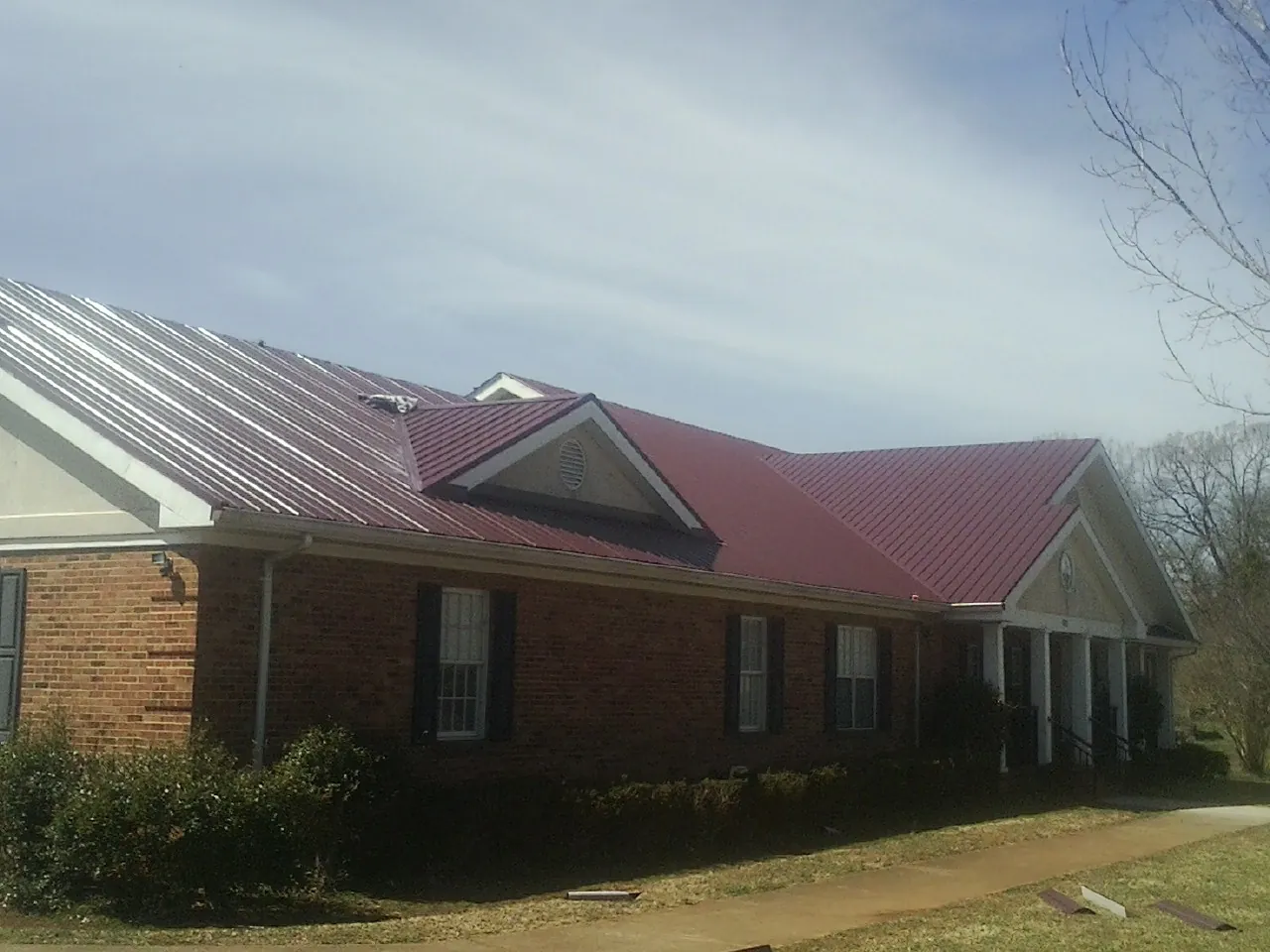 Red metal roof with gabled entries on a long brick building, from a Hail Damage Roof Repair job in Mabelvale