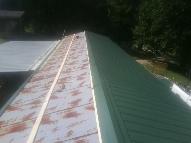 Old rusted panels beside newly installed green metal roofing — Wind Damage Roof Repair by Roofing Brothers in Mabelvale