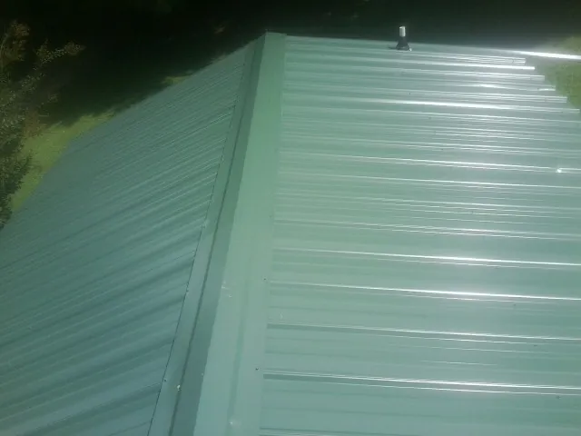 New green metal panels meeting at the ridge of a roof — Flat Roof Repair work by our crew in Mabelvale