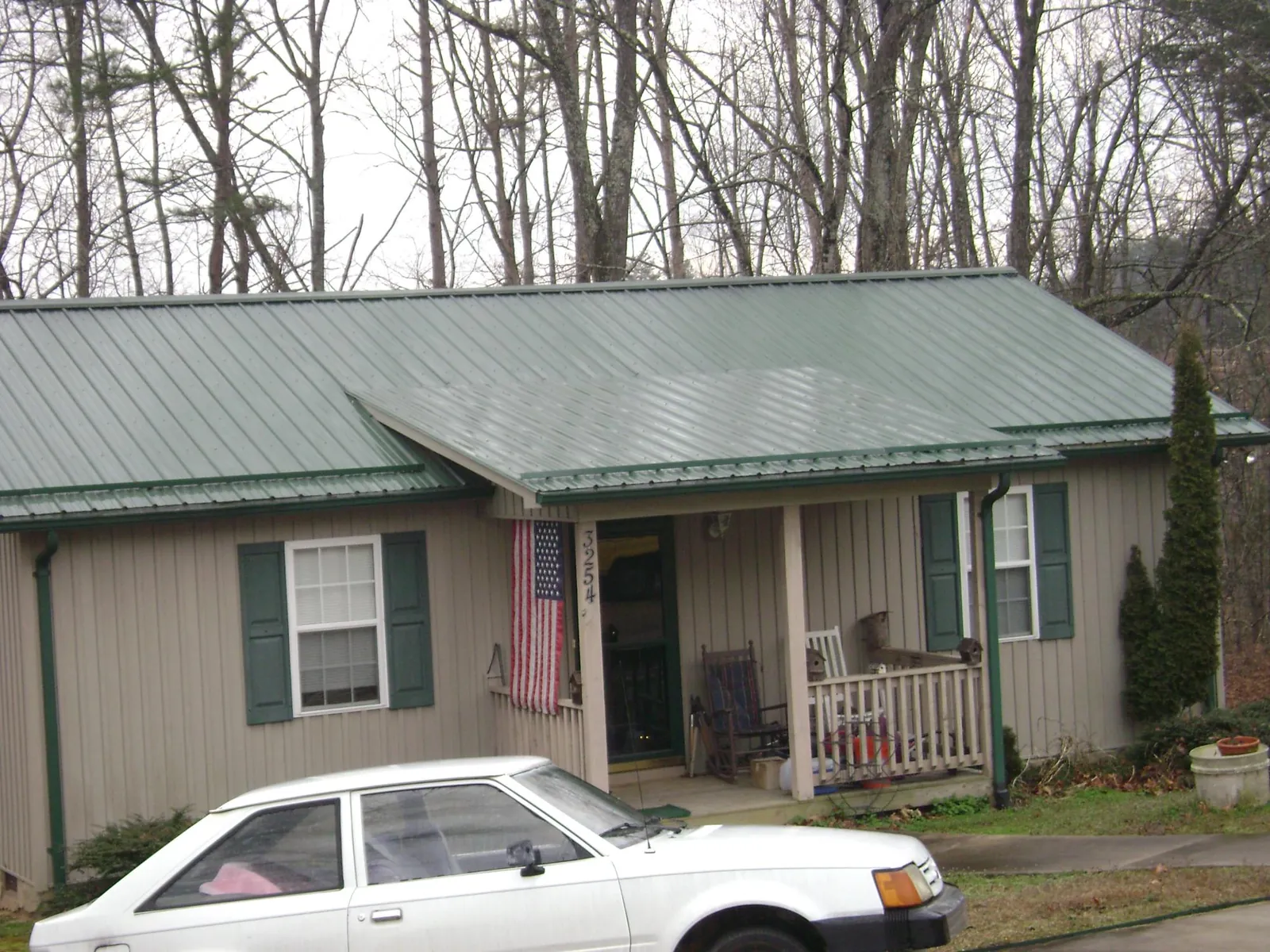 Green metal roof and front porch on a tan sided cottage in Mabelvale