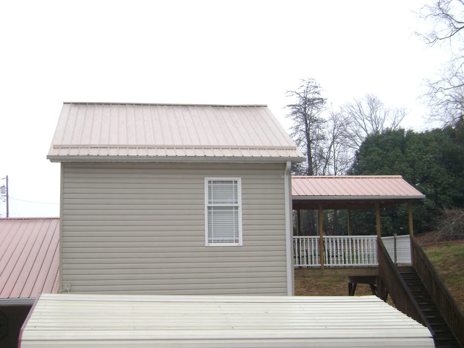 Tan metal roofs on a two story addition and attached porch, from a Roof Replacement job in Mabelvale